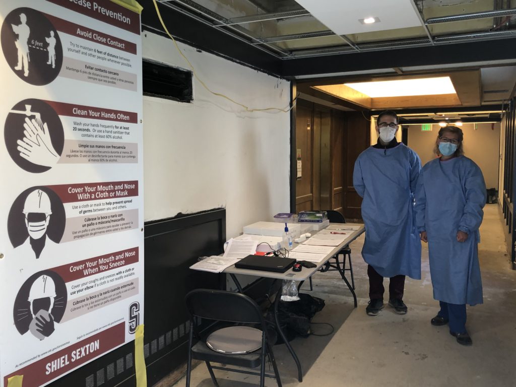 Two medical professionals stand beside Shiel Sexton COVID-19 safety signs